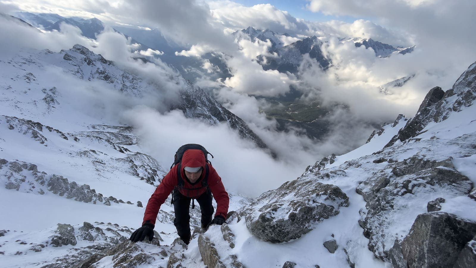 Alpiniste franchissant un ressaut rocheux au-dessus d'une mer de nuages